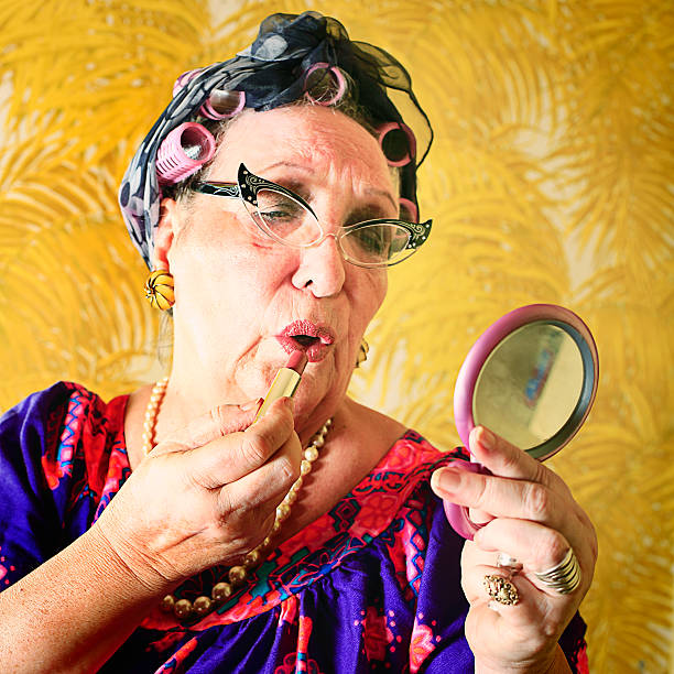 A crazy granny in curlers and cat's eye glasses putting on her makeup. More granny images.